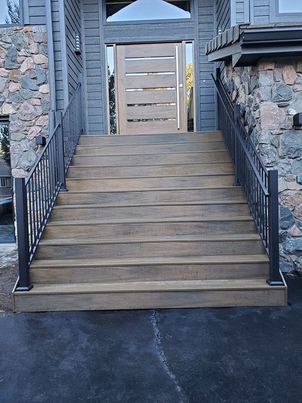 Wooden steps leading to a front door with metal railings, dark exterior.