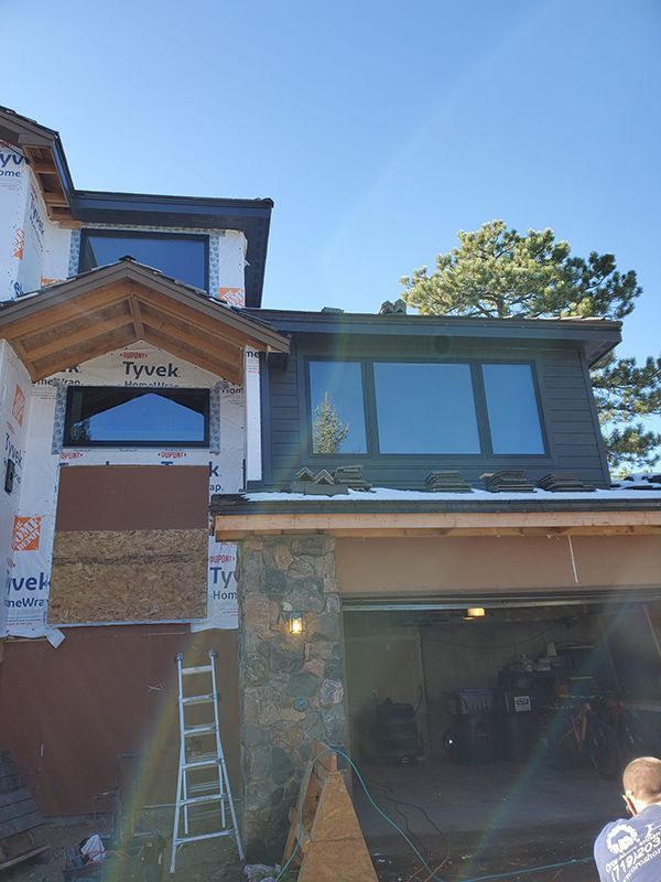 Exterior of a house under construction; dark siding, stone accents, garage, windows, Tyvek wrap, blue sky.