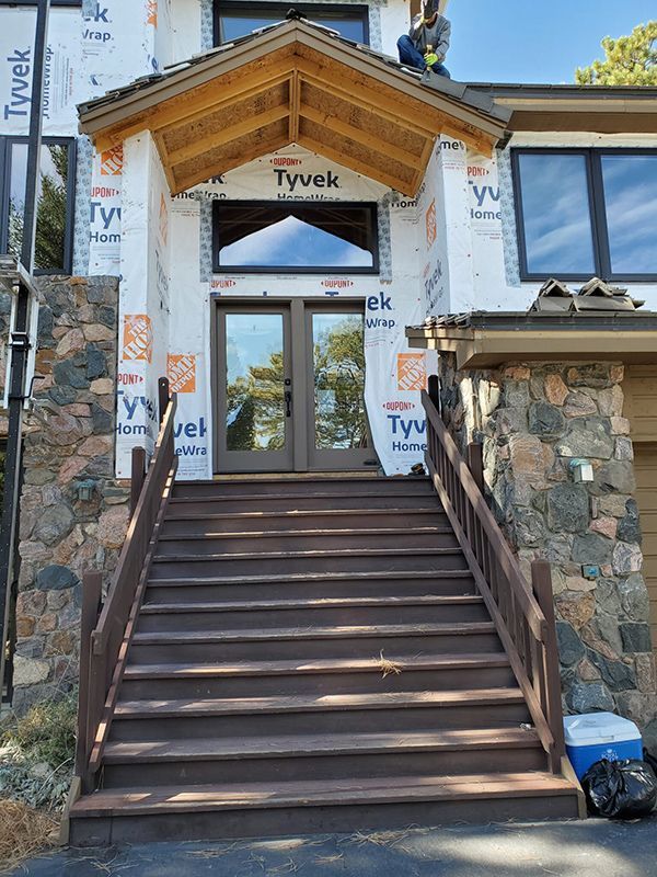 House entrance with stone facade, brown stairs, double doors, and a worker on the roof.