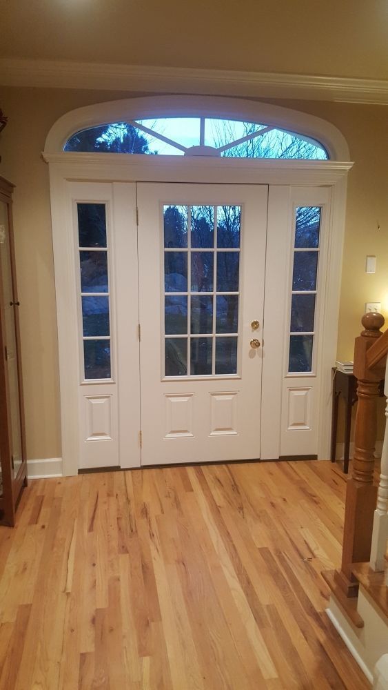 White paneled front doors with side panels and arched transom window. Hardwood floor.
