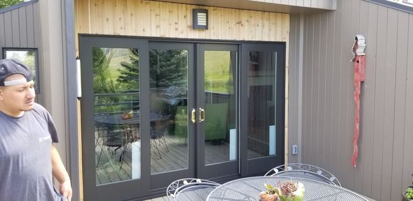Man stands outside a house with black-framed glass doors, patio table, and outdoor artwork.