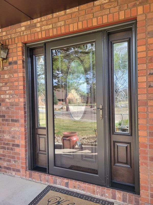 Brick building entrance with black-framed glass door and sidelights; a doormat sits on the concrete porch.