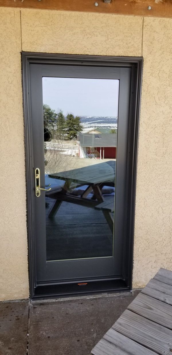 A dark gray door with a glass pane reflects an outdoor scene with a picnic table, building and sky.