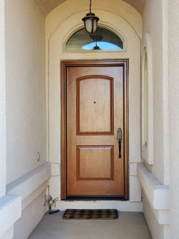 Wooden front door with arched transom window, centered in a beige alcove with a hanging light.