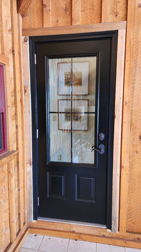 Black front door with glass panels and a grid, set in a wooden frame.