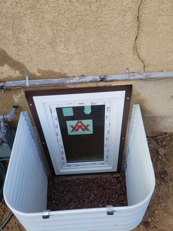 Basement window well with a new window, gravel, and white plastic sides, against a beige stucco wall.