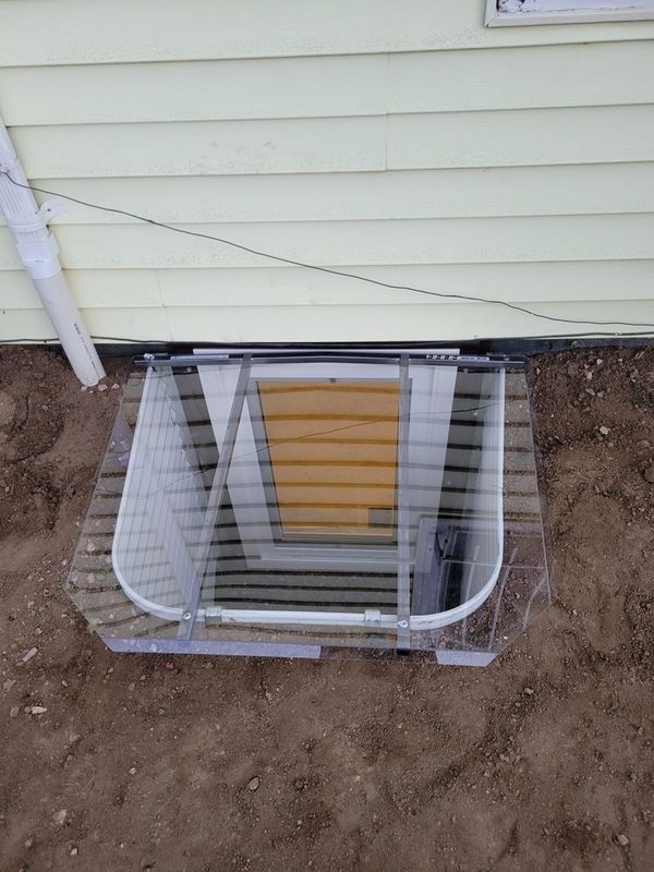 Window well with clear plastic cover on a house exterior.