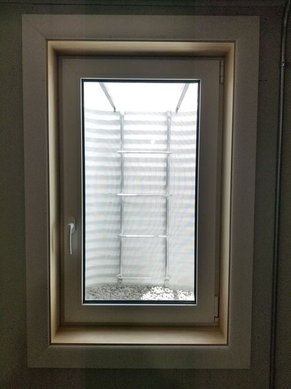 White-framed basement window, light shining through. Window well visible.