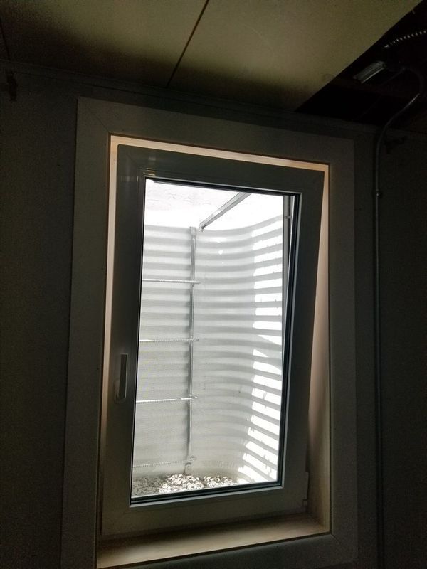Window in a basement with a window well. The window has white trim and is slightly ajar.