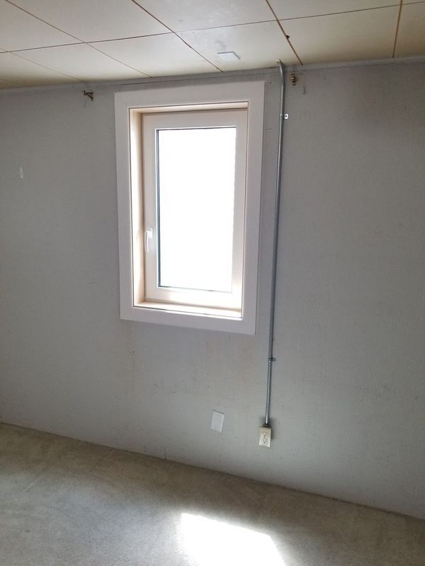 Window in a room with light gray walls, a concrete floor, and a cable running down the wall.