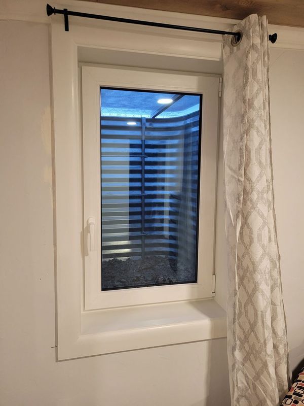White framed window with sheer curtain, black rod. The window has light filtering blinds.