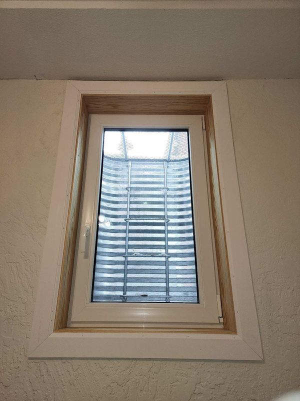 White-framed basement window with a curved window well. Trim is white and light wood.