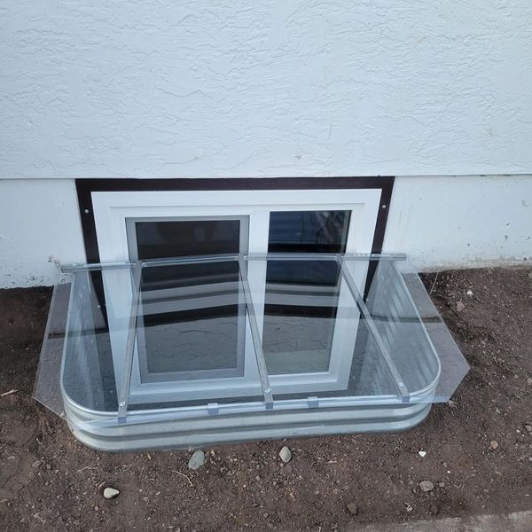 Basement window with clear well cover; white exterior wall.
