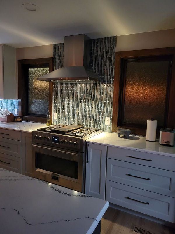 Kitchen with stainless steel range, blue mosaic backsplash, and white cabinets.