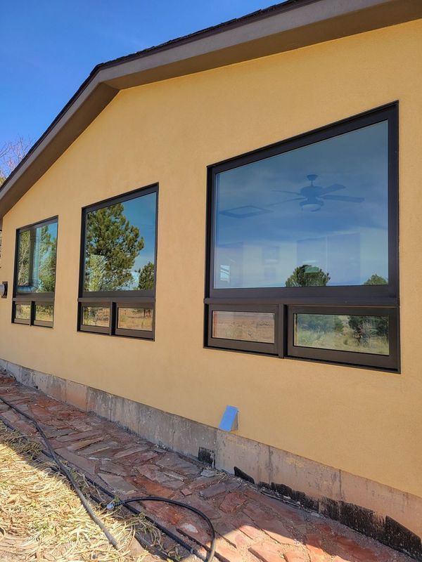 Yellow house with black-framed windows reflecting the sky, set on a foundation, with a brown roof.