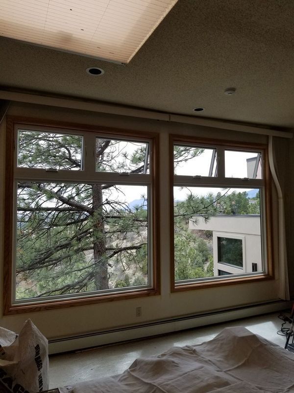 Two large windows offer a view of trees and a building outside. Brown trim, white interior, light-colored walls.