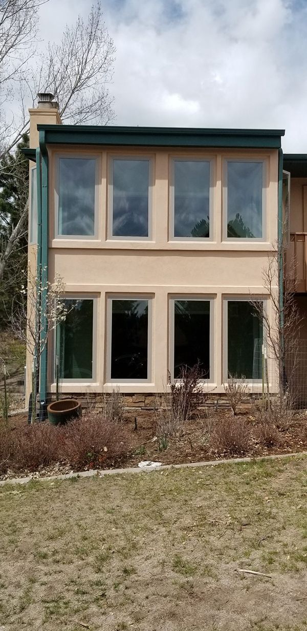 Tan building with large windows, green trim, and stone base. Overcast sky and bare trees.
