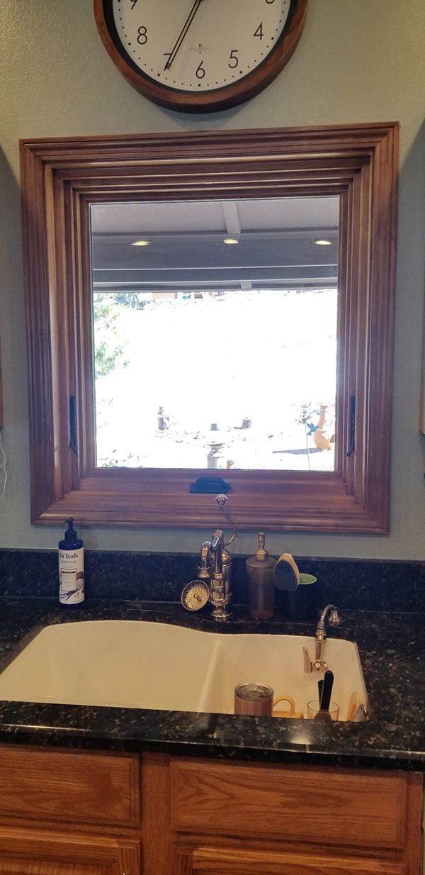 Bathroom sink with a mirror and clock. Brown wood frame, gold faucet, and black countertop.