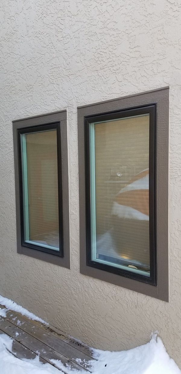 Two windows with dark trim on a textured, light-colored wall, snowy ground below.