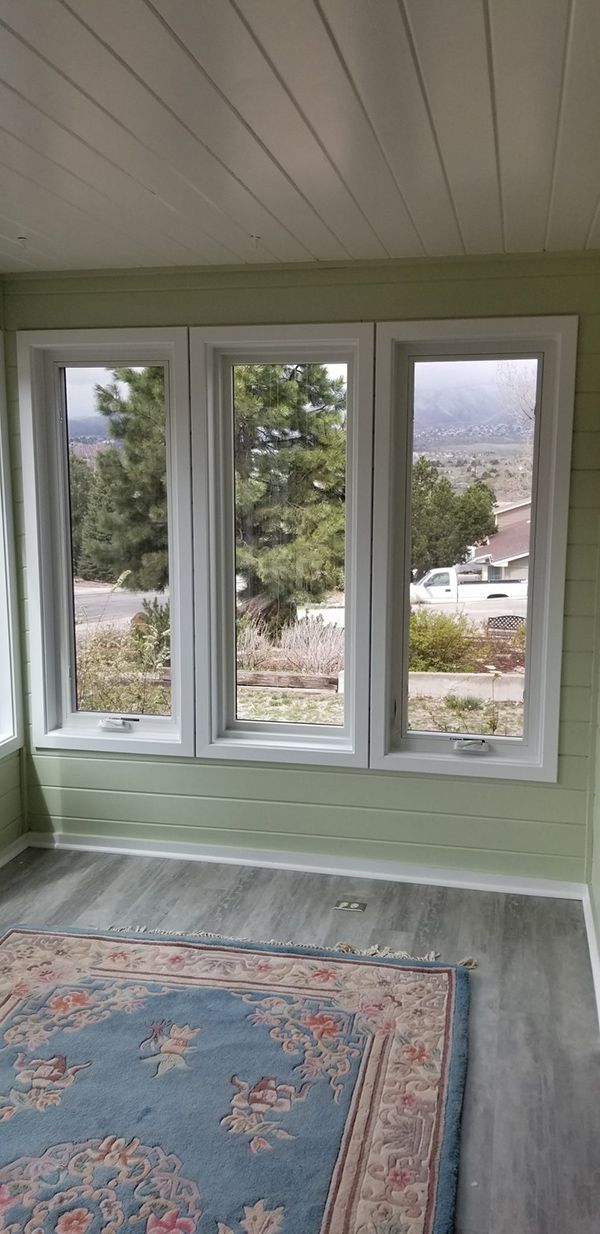 Three white-framed windows overlooking a landscape. Green walls and rug, light gray floor, and white paneled ceiling.