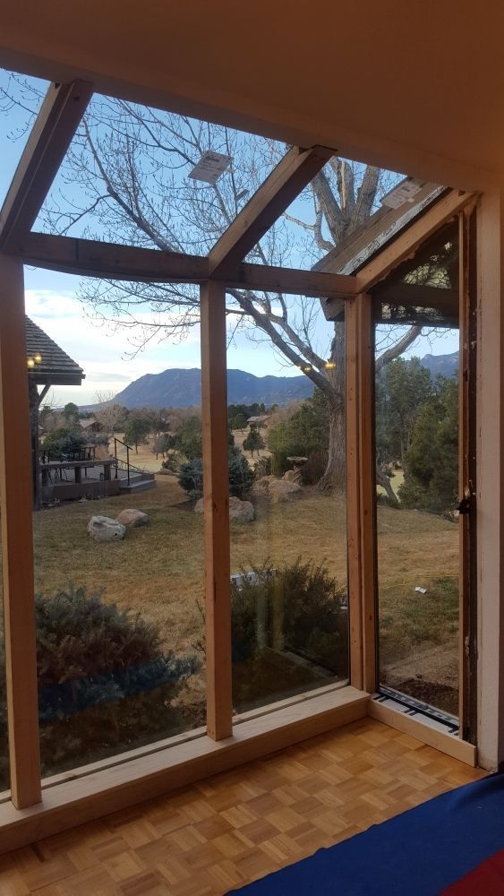 Sunroom with wooden frames and glass panels, overlooking a landscape with a mountain view.