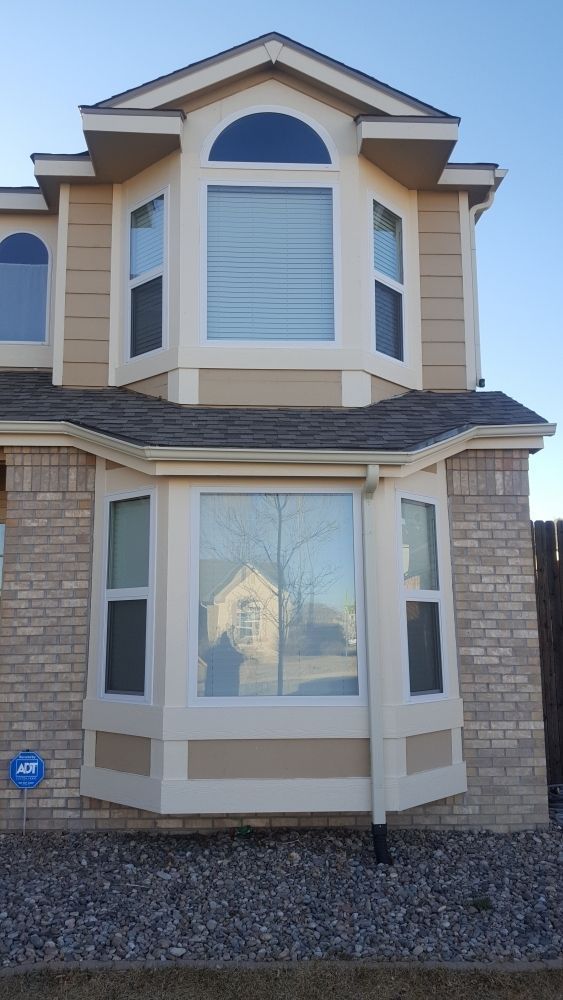Two-story house with tan siding, bay windows, and a brick facade.