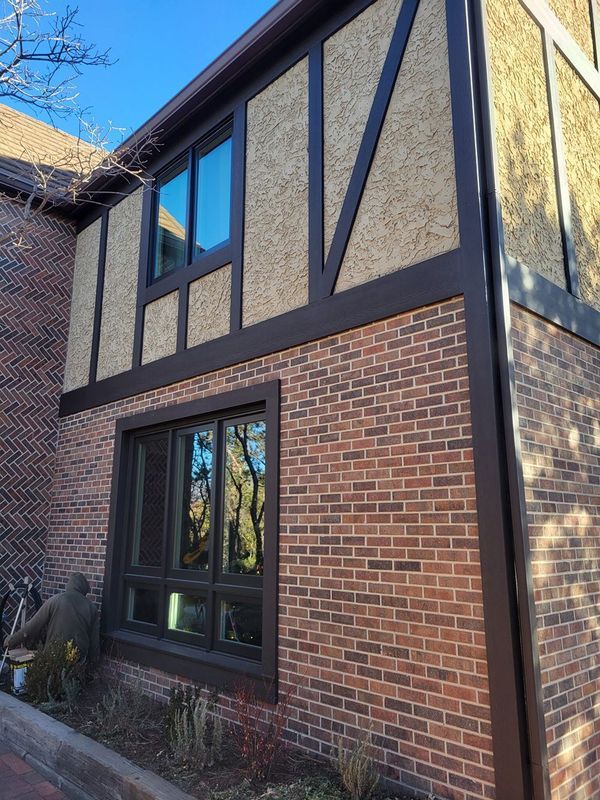 Brick building corner with brown trim and windows. Beige textured stucco and a glimpse of tree reflections.