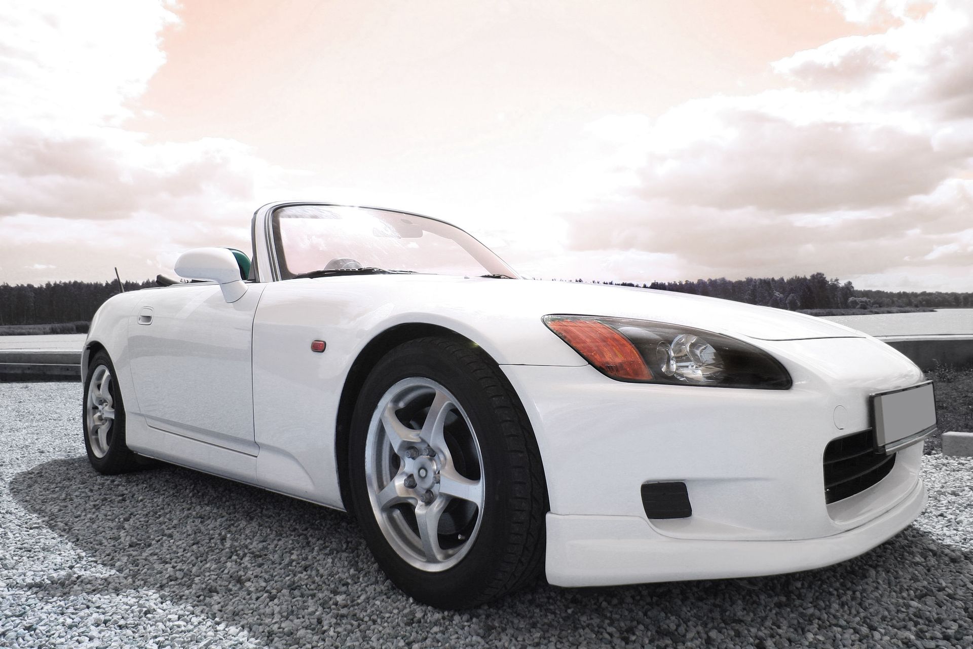 White convertible car parked on gravel, against a cloudy sky.
