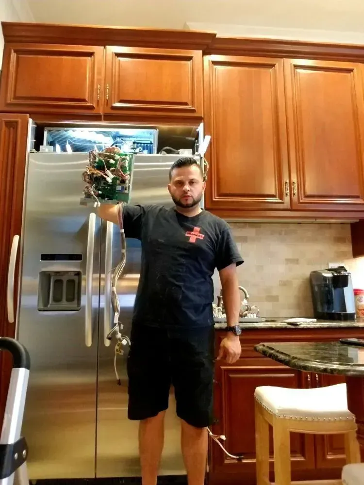 Man holding part of a refrigerator in a kitchen with brown cabinets.