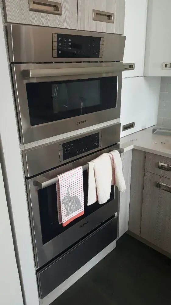 Stainless steel built-in oven stack in kitchen with hand towels hanging on the oven handle.