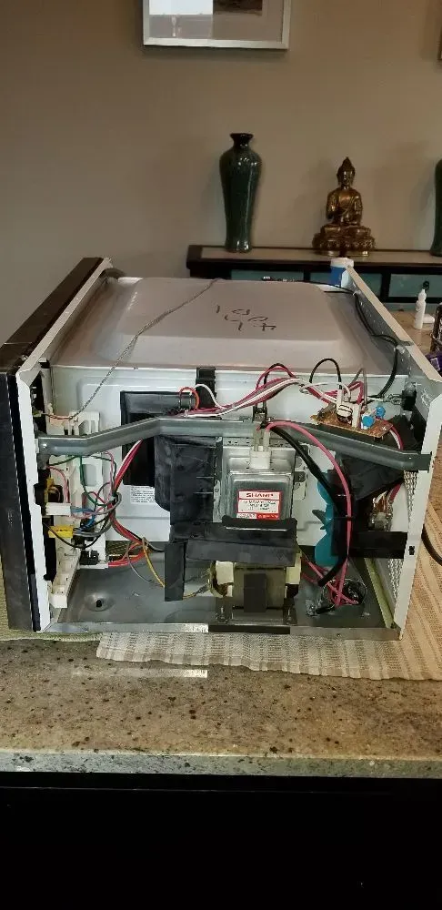 Microwave with the cover off, revealing internal wiring and components. It sits on a speckled countertop.