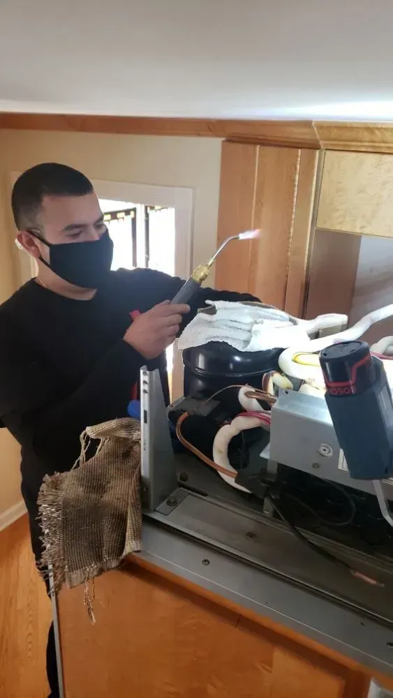 Man in black mask using a torch on HVAC equipment. Indoors, wooden paneling visible.