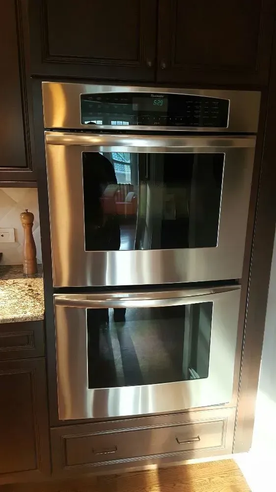 Stainless steel double oven built into dark wood cabinets.