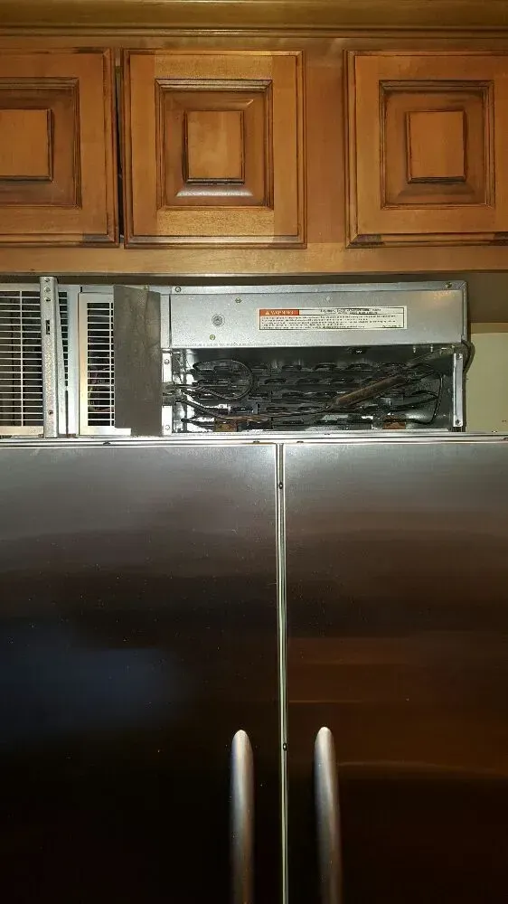 Stainless steel refrigerator beneath kitchen cabinets with vent.