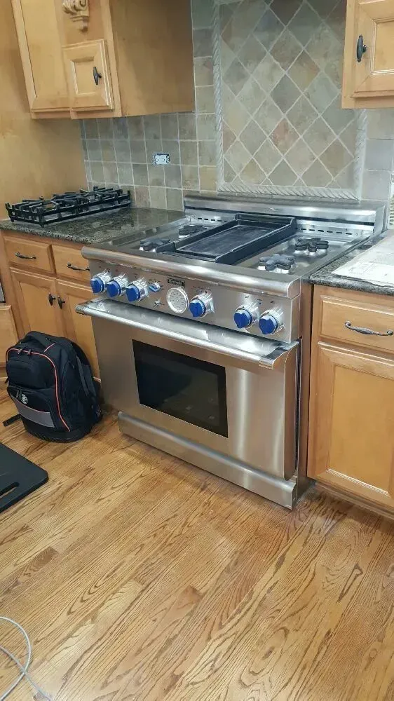 Stainless steel oven with gas cooktop in a kitchen. Wooden cabinets, hardwood floor.