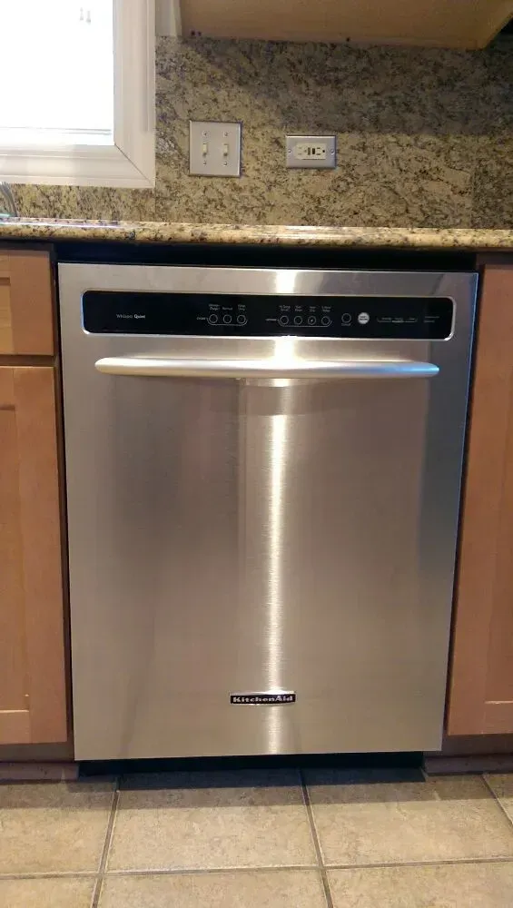 Stainless steel KitchenAid dishwasher in kitchen with light-colored cabinets, beige countertop, and tile floor.