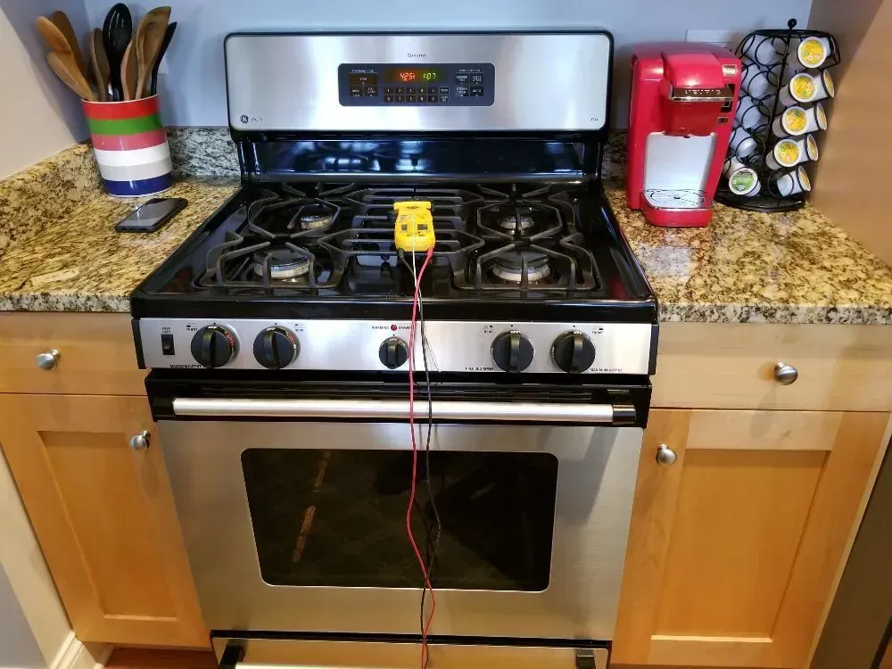 Gas stove with yellow thermometer, red K-cup coffee maker, and stainless steel appliances on granite counter.
