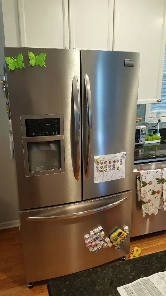 Stainless steel refrigerator with butterfly magnets on the door in a kitchen.