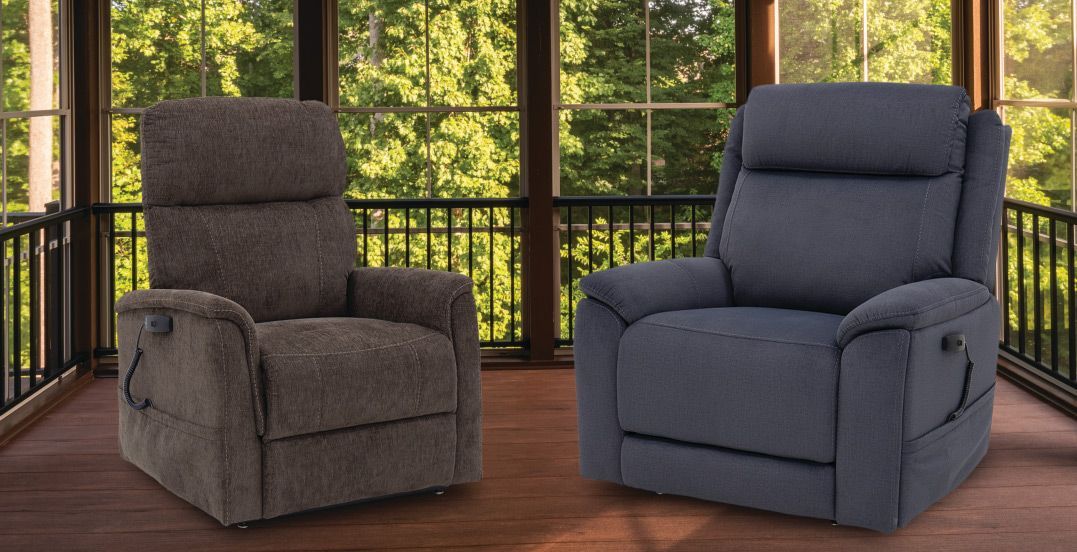 Two recliner chairs, one brown and one blue, stand on a wooden porch in front of a windowed wall with outdoor greenery.