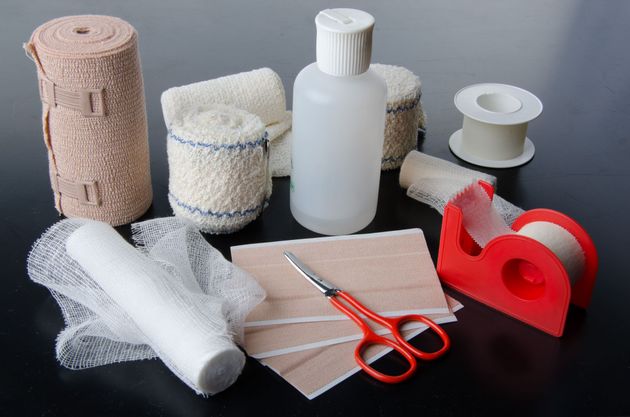 A collection of first aid supplies, including bandages, medical tape, a bottle of liquid, and orange scissors on a table.