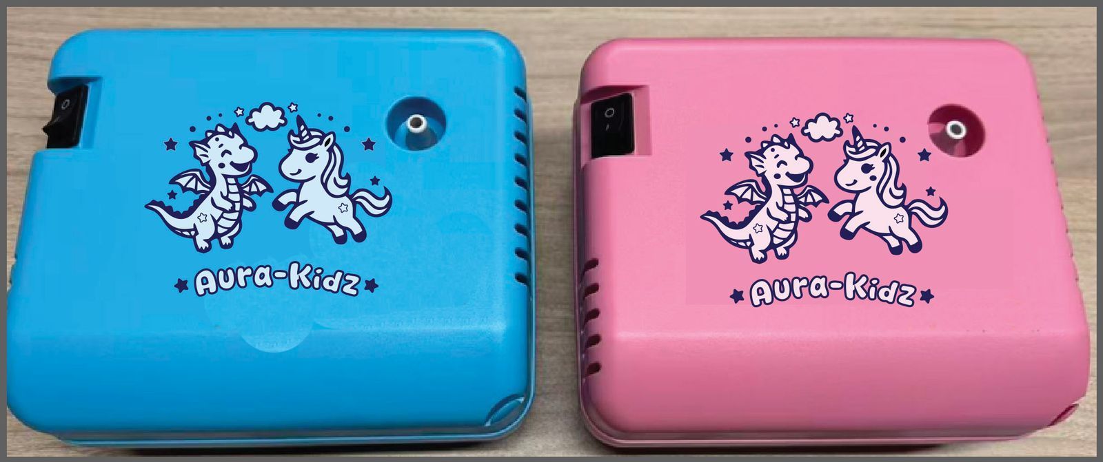 Two portable Aura-Kids nebulizers, one blue and one pink, featuring a cartoon dragon and unicorn graphic on the front.