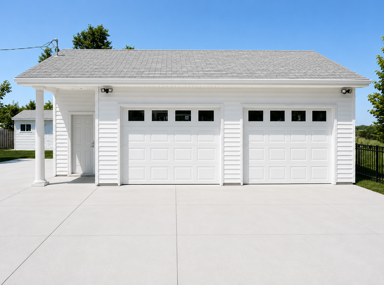 White double garage with two doors and a large concrete driveway under a blue sky