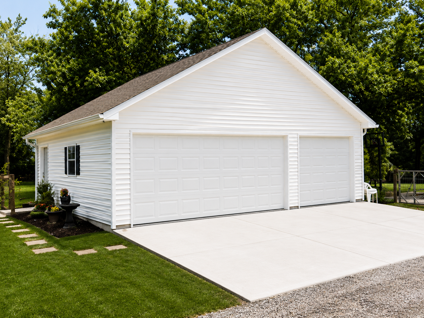 Two-car white garage with concrete driveway; set in a yard, trees in the background.