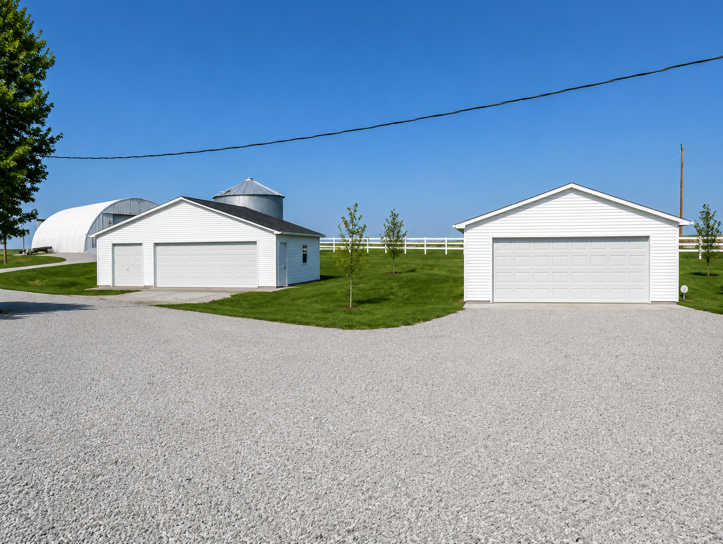 Two white garages on a gravel lot under a clear blue sky, with a grassy strip between them.