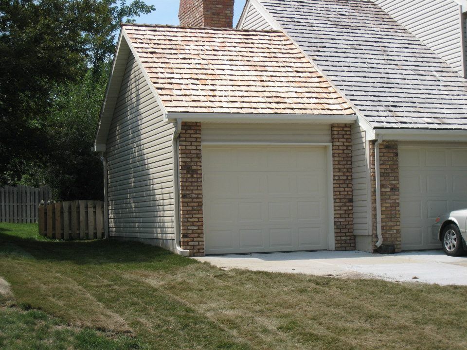 Garage with beige door, brick accents, and cedar shake roof. Beige siding, green lawn.