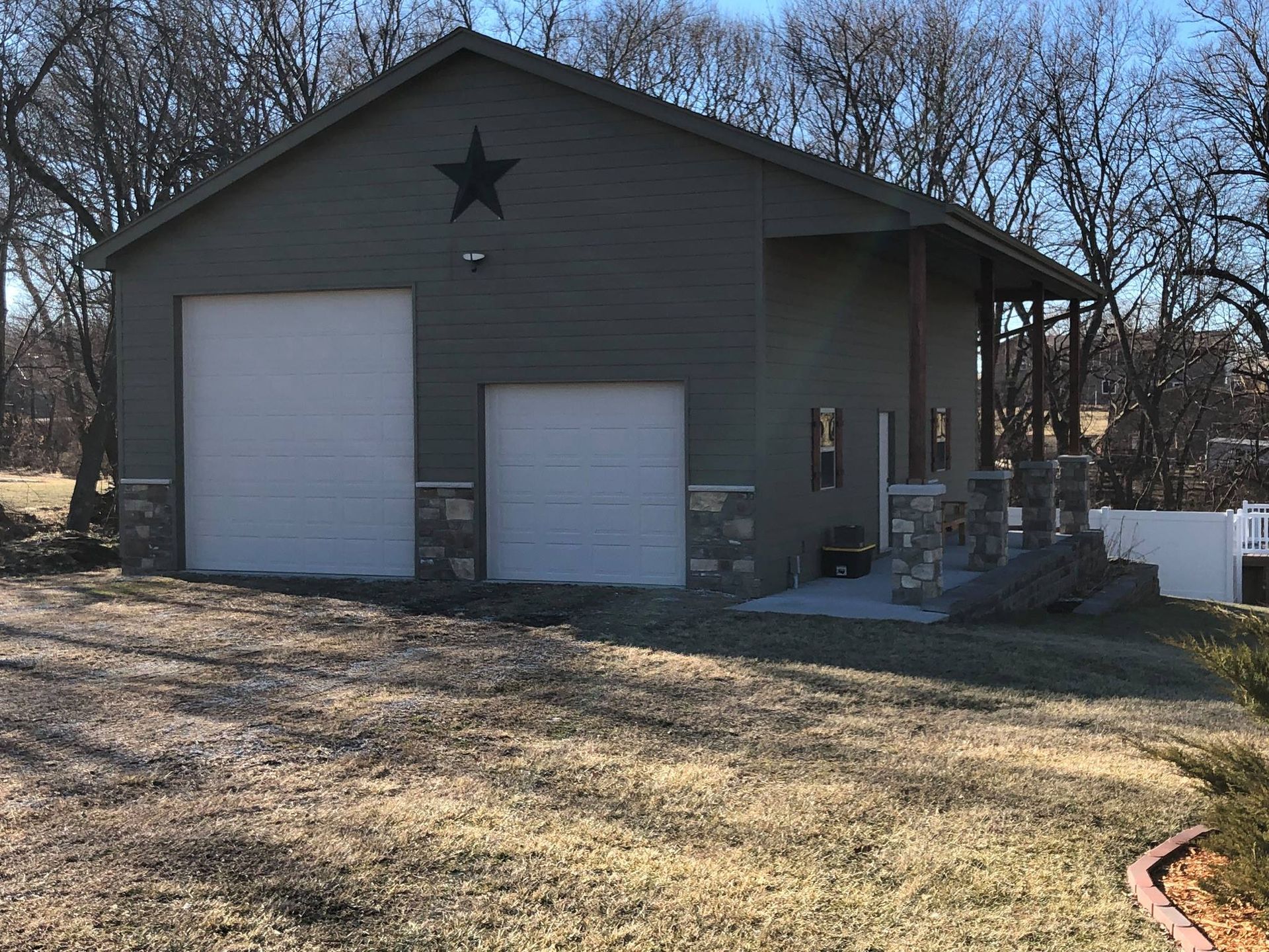 Green garage with white doors, porch, and a black star. Set in a grassy yard.