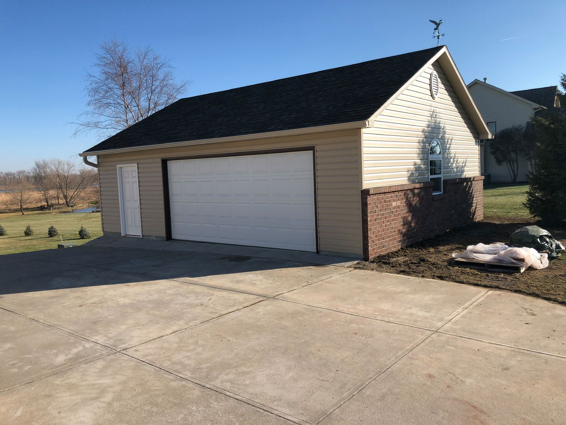 Tan garage with black roof and white garage door, on a concrete driveway.