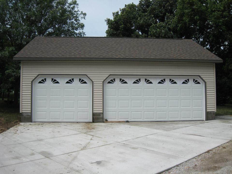 Tan two-car garage with a brown roof and white garage doors on a concrete driveway.