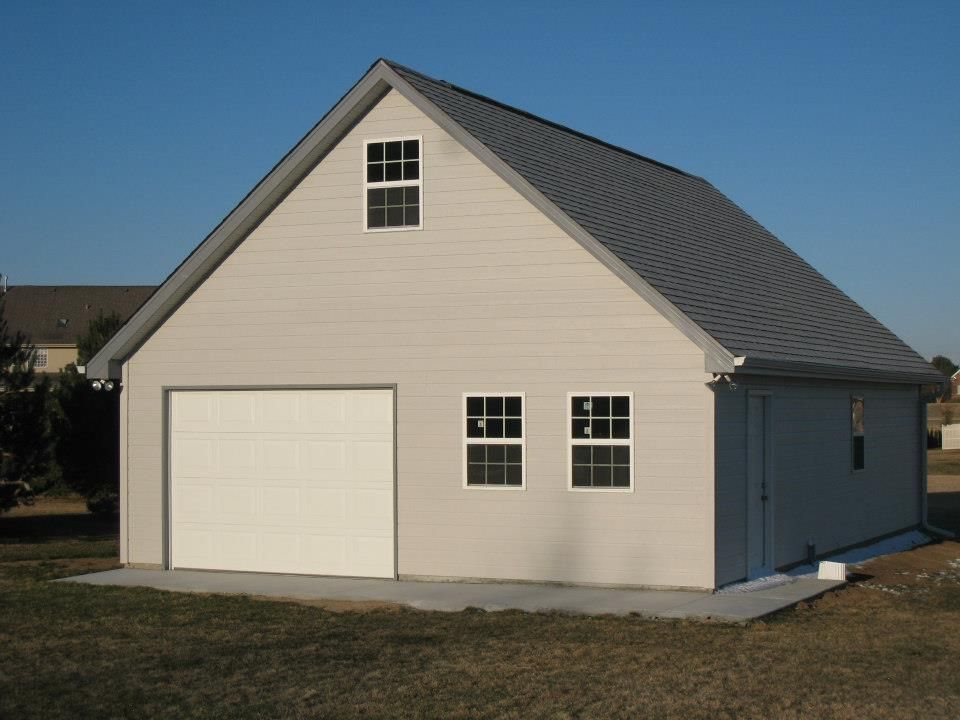 Light gray two-story garage with white garage door, windows, and dark gray roof against a clear blue sky.