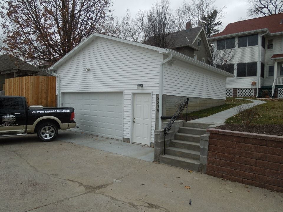 White garage with two bays, a side door, and steps leading to a sidewalk. A truck is parked to the left.